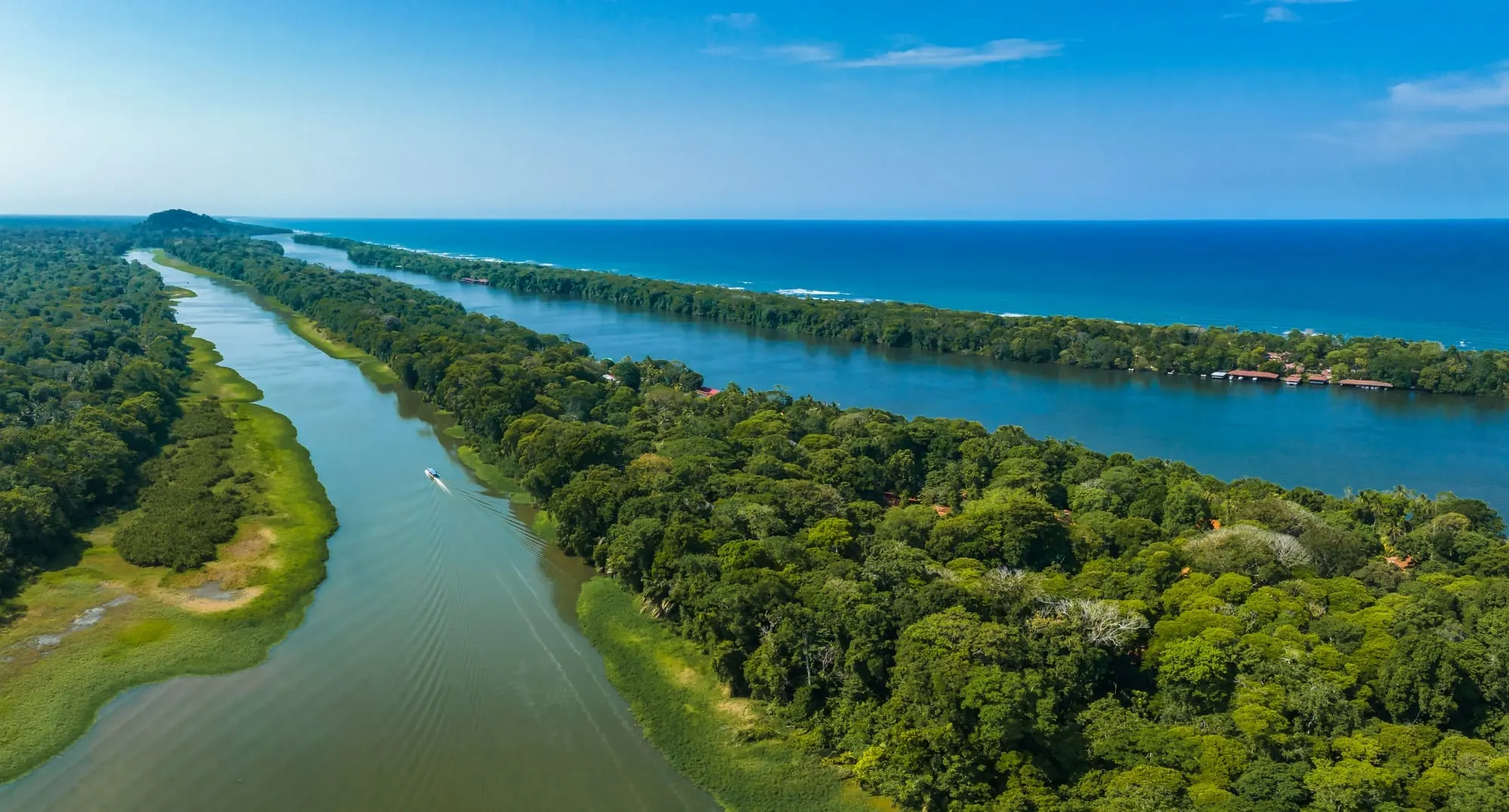Vista aérea de los canales de Tortuguero, la selva y el Caribe; un bote navega el río